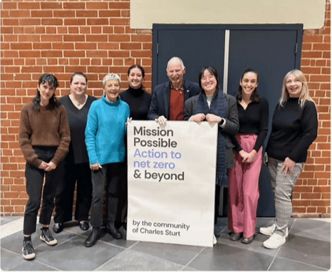 Eight Mission Possible members standing with a sign reading 'Mission Possible — Action to net zero & beyond, by the community of Charles Sturt'.